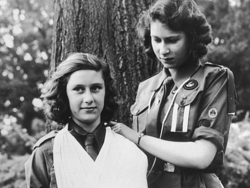Королева Великобритании Елизавета II со своей сестрой Маргарет в 1943 году. Они принимали участие в Первой кампании женской организации скаутов Букингемского дворца. Две полоске на ее униформе свидетельствуют о том, что она руководитель отряда скауто