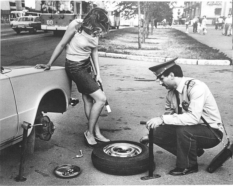 Сотрудник ГАИ помогает девушке с заменой колеса. СССР. 1980-е. 