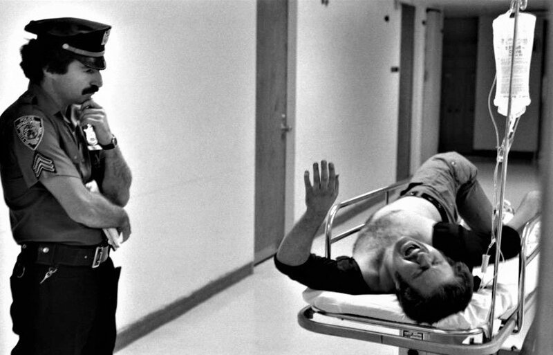 Полицейский терпеливо ждет в приемном покое госпиталя, пока раненная в ногу жертва расскажет ему, что произошло, 1978 год. 