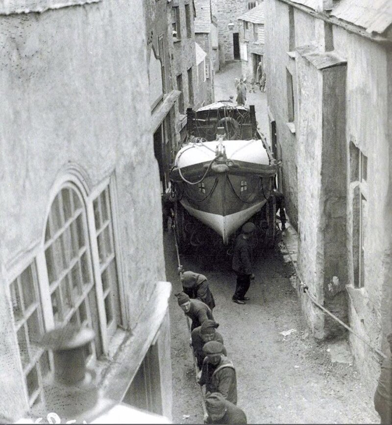 Моряки тянут лодку по узким улочкам городка Порт Исаак от места постройки для спуска на воду. Англия, 1928 год 