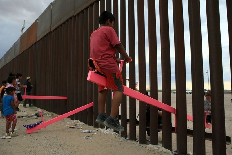17. Дети из США и Мексики катаются на качелях, установленных на границе стран