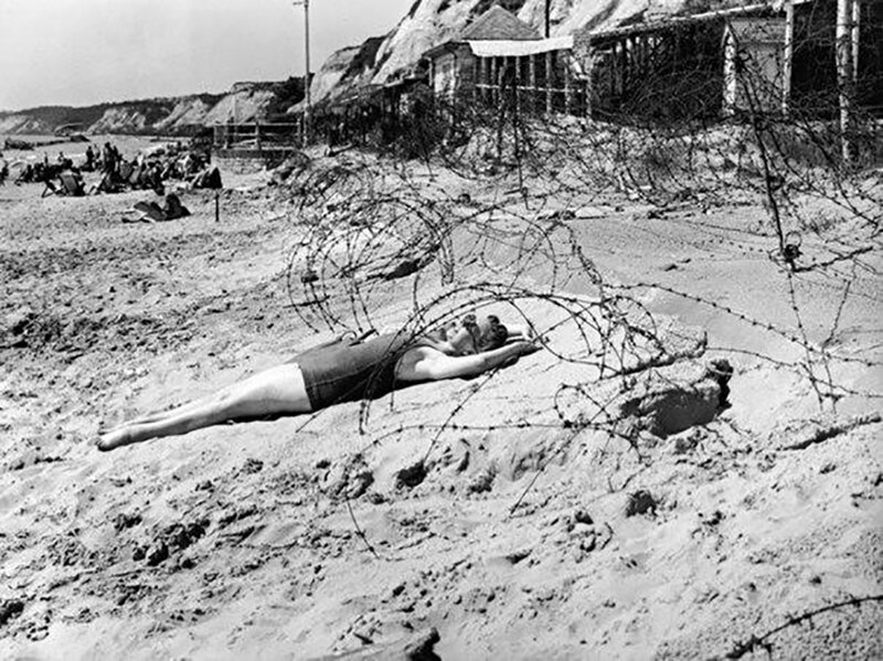 Женщина загорает в военное время в окружении колючей проволоки на пляже в Борнмуте, 1944 г.