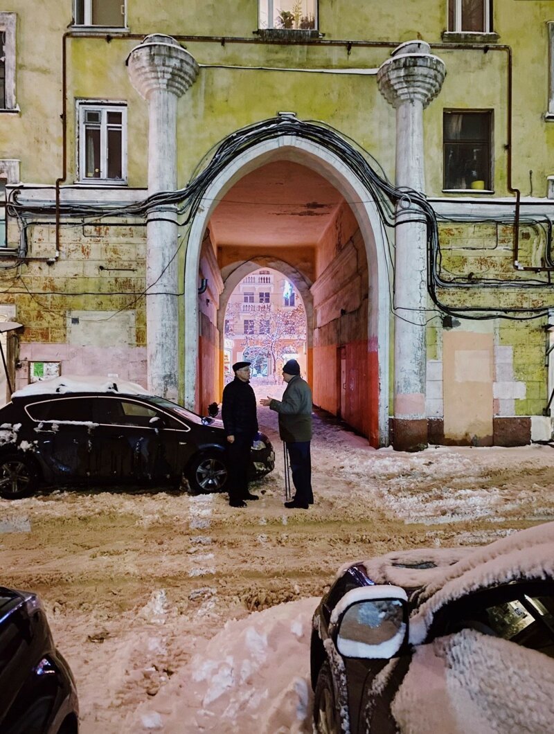 Двое мужчин общаются поздно вечером во дворе здания сталинских времен. 
