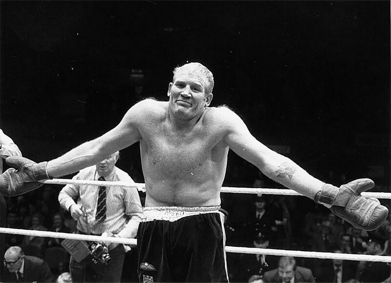 Ричард Данн, боксер на боксерском ринге, пожимает плечами в извинениях к зрителям. 1975 