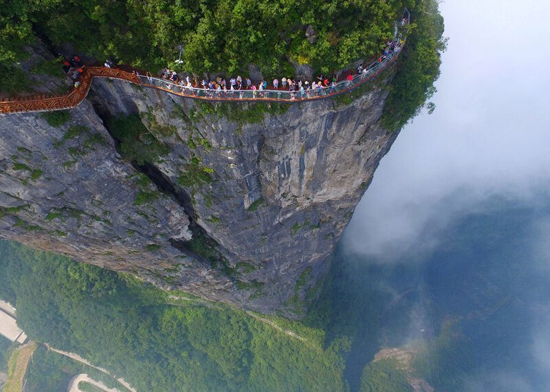 Туристы стоят на дорожке с стеклянным полом, наверху огромной скалы, в Чжанцзяцзе, провинция Хунань, Китай.