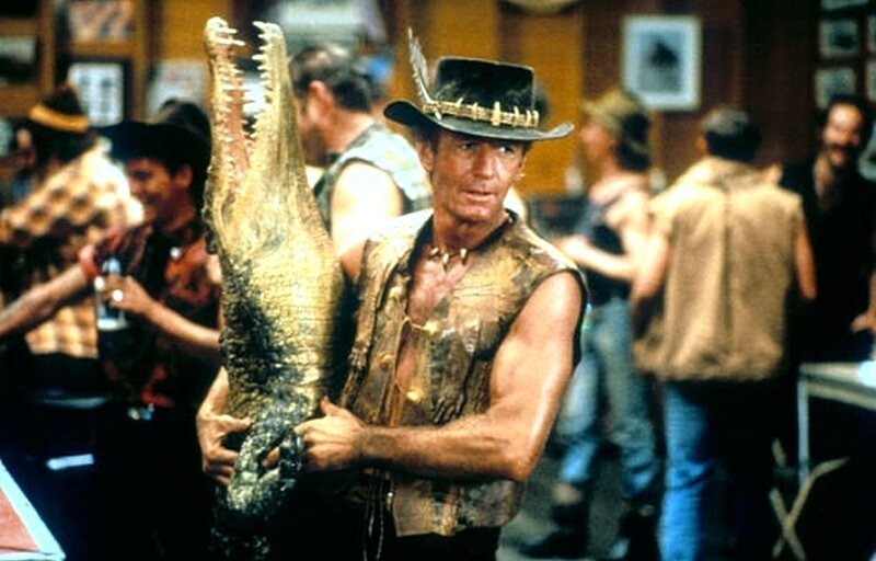 Пол Хоган несет мертвого крокодила  в сцене в баре из фильма «Крокодил Данди», 1986 год.
