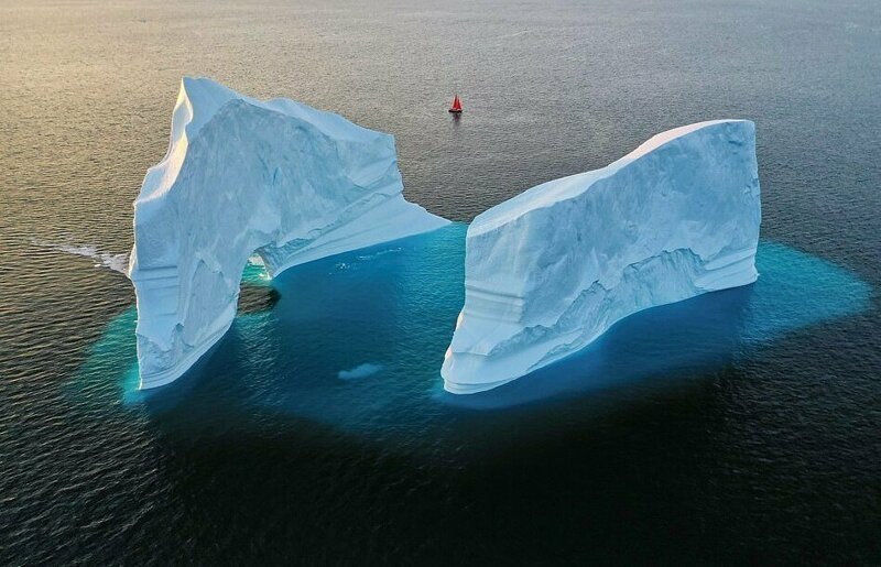 Крошечная лодка проплывает возле огромного айсберга