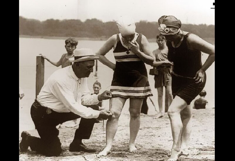 Мужчина измеряет длину женских купальных костюмов в 20-х годах прошлого века. Если они будут слишком короткими, то женщин оштрафуют.