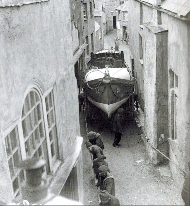 Моряки тянут лодку по узким улочкам городка Порт Исаак от места постройки для спуска на воду. Англия, 1928 год.