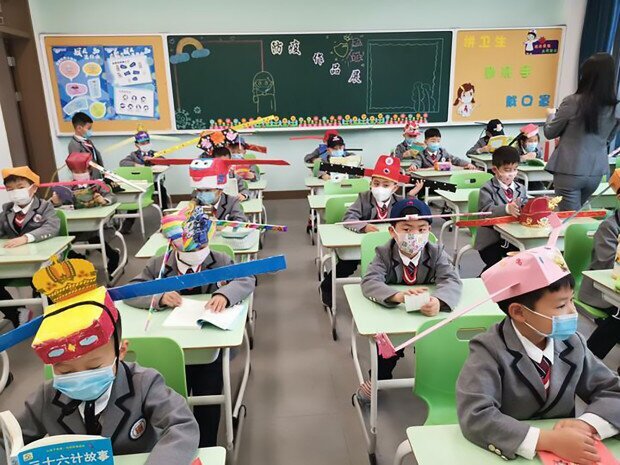 Китайские младшеклассники посещают уроки в масках и самодельных шляпах, помогающих соблюдать дистанцию