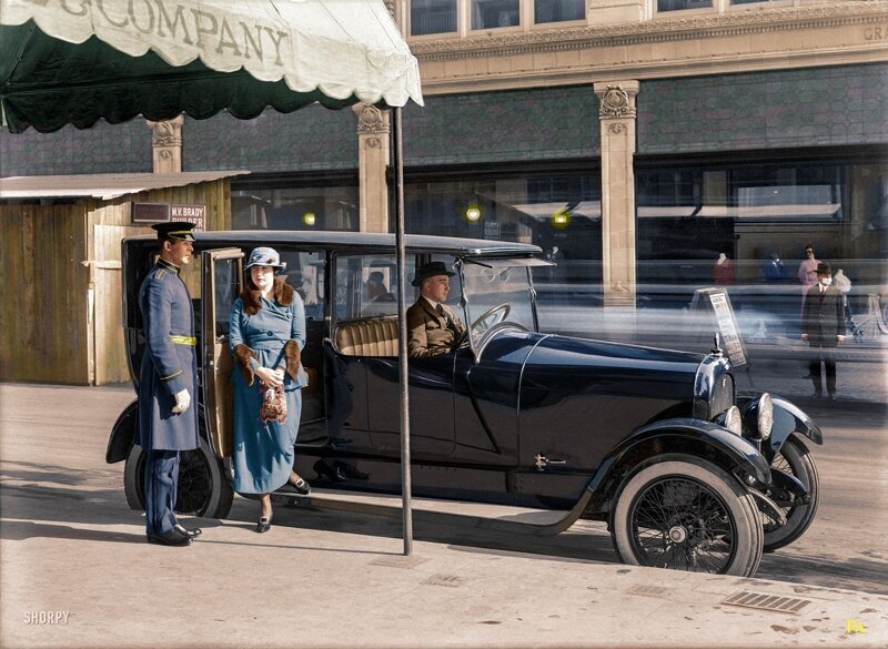 Дормен открывает дверь даме выходящей из автомобиля марки Marmon. На другой стороне улицы можно заметить джентльмена в медицинской маске. Сан-Франциско, 1919 год.