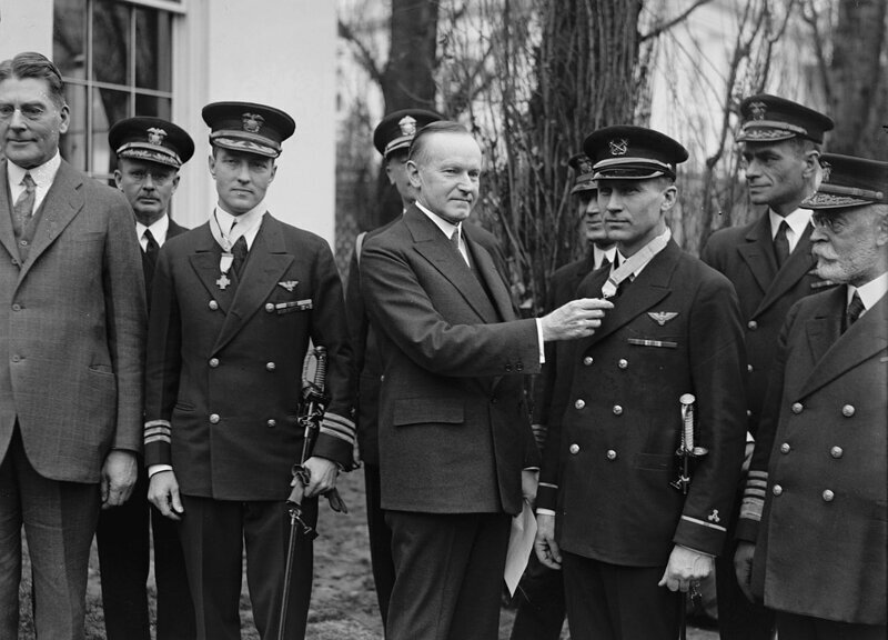 Президент США Калвин Кулидж награждает Почетной медалью Конгресса США прапорщика Флойд Беннетт (справа) и командира Ричард Э. Бэрда (слева) за первый полет над Северным полюсом, совершенным 9 мая 1926 года. 19 февраля 1927