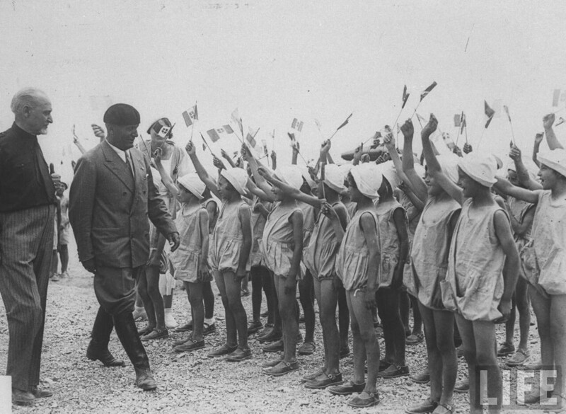Бенито Муссолини проходит мимо группы маленьких девочек, размахивающих флагами во время посещения недавно мелиорированных Понтийских болот. 1930