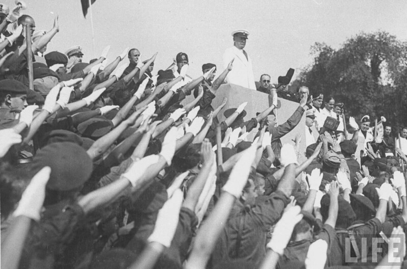 Бенито Муссолини стоит на подиуме во время посещения испанского военного лагеря. Испания