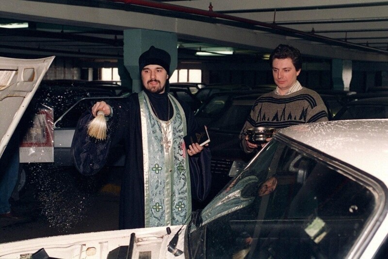 Православный священник за 20 баксов окропляет святой водой новый автомобиль «Лада», только что проданный в салоне одного из московских дилеров, 1995 год.