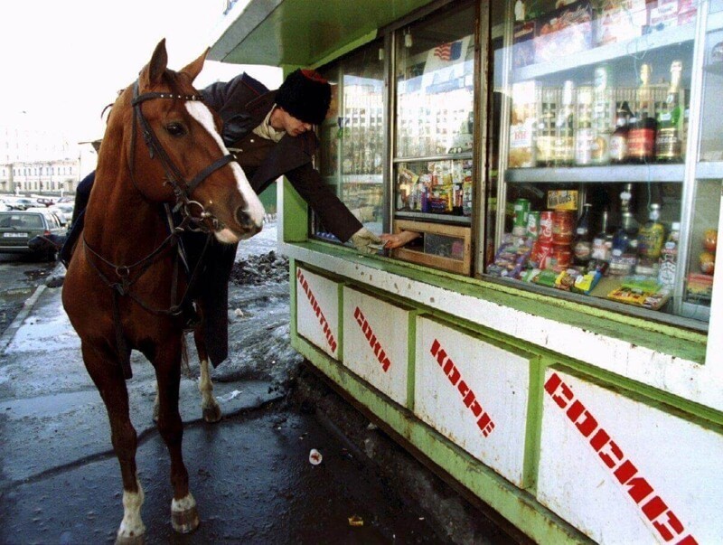 Казак на лошади покупает водку в киоске во время парада в честь дня Святого Патрика в Москве. Мероприятие, не являющееся традиционным для России, было спонсировано сообществом иностранных бизнесменов, март 1994 года.