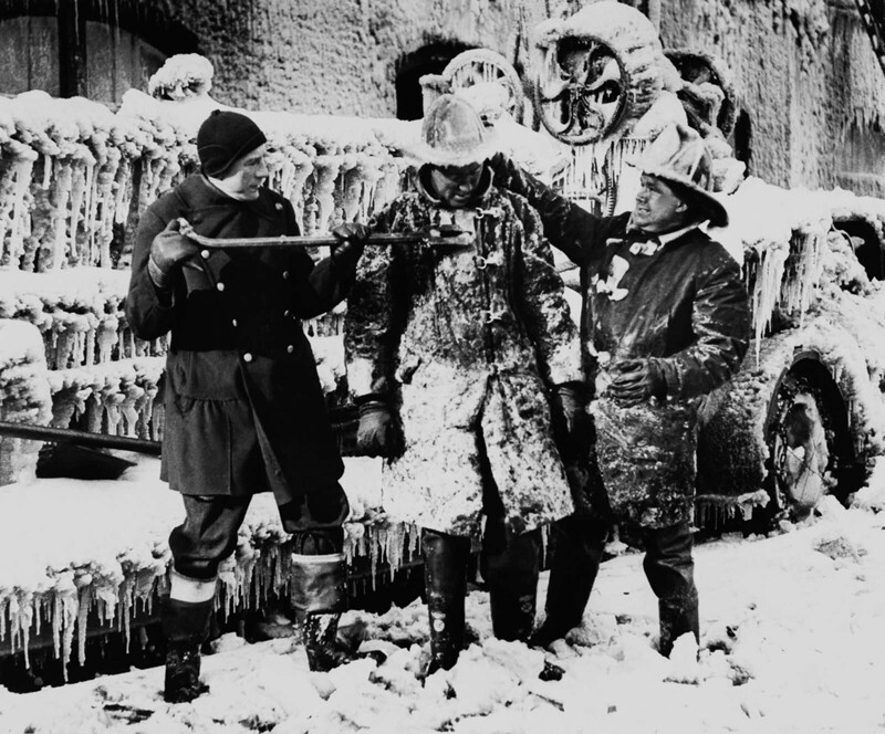 Пожарные Нью-Йорка помогают коллеге сбивать лед с формы. 1936 г.