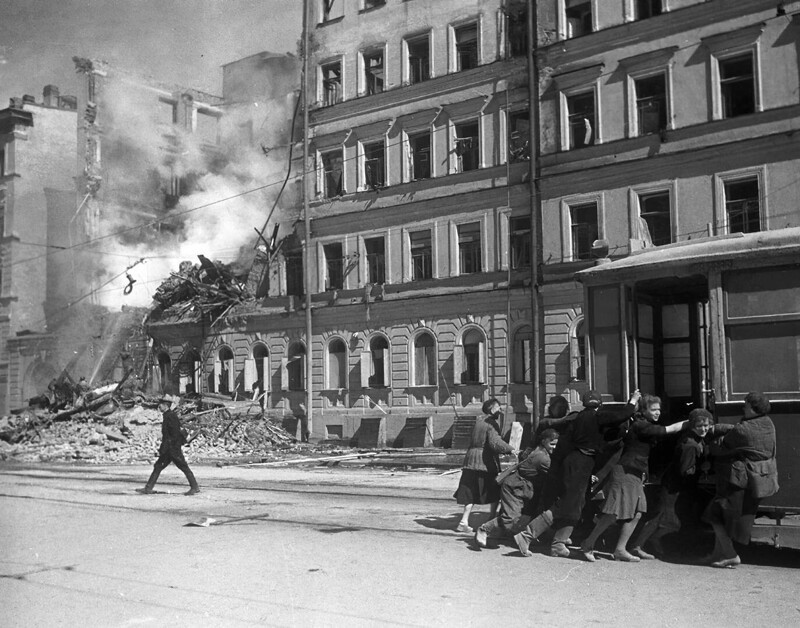 Жители блокадного Ленинграда передвигают трамвайный вагон подальше от фасада разрушенного бомбардировкой дома. 1942 г