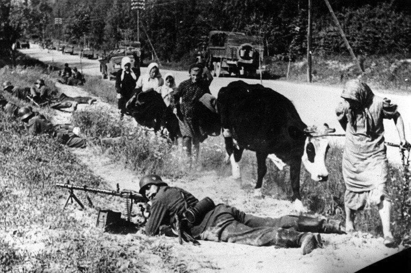 Беженцы с коровой проходят мимо немецкого пулеметчика. Где-то в Укрaине, 27 июня 1941 год