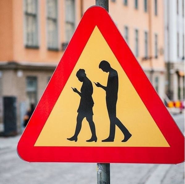 Дорожный знак предупреждает водителей, что они могут столкнуться с пешеходами, которые глубоко поглощены своими смартфонами, в Стокгольме, Швеция