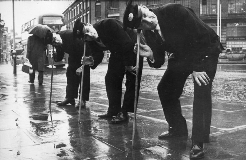 Три инспектора по подземным водам проверяют с помощью ясеневых тростей возможные места утечек в трубах под Розвери-роуд. 1966 год, Лондон, Англия
