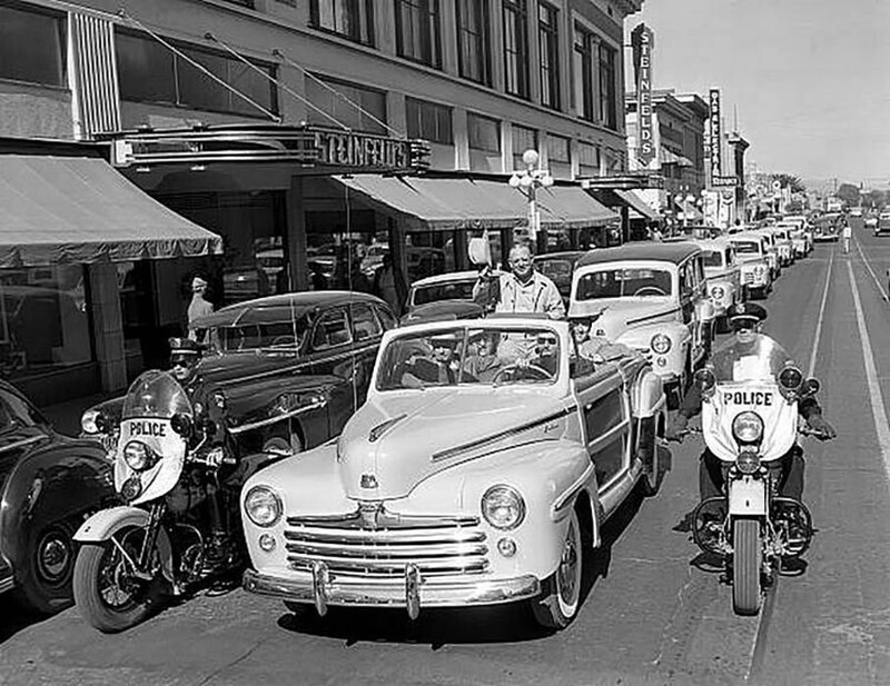Ford Super DeLuxe 11. 1947 года с откидным верхом ведет парад новых автомобилей Ford перед универмагом Штайнфлед на Стоун-авеню в Тусоне, штат Аризона.