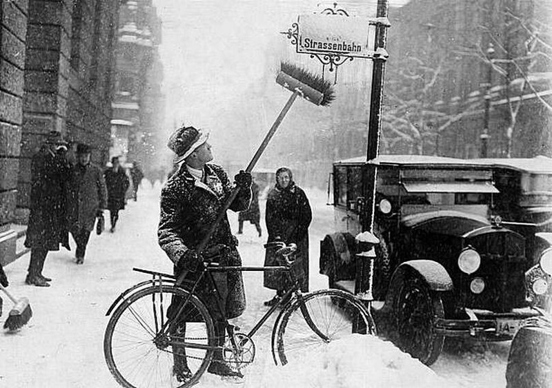 Мужчина на велосипеде и со щёткой сметает снег с уличного знака в Берлине - 1929