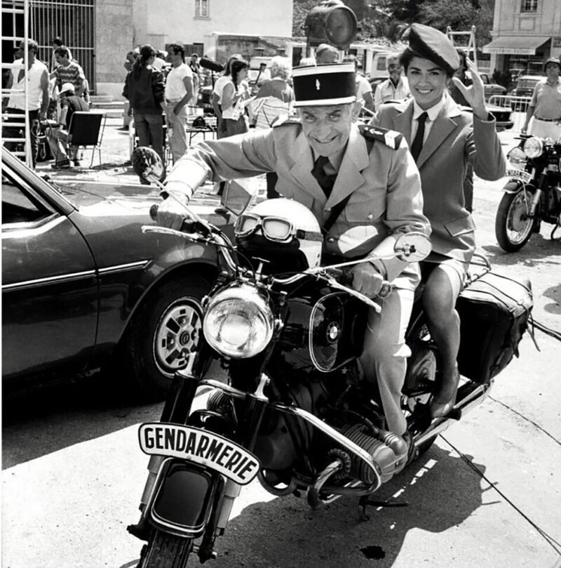 Луи де Фюнес на съёмках кинокомедии «Жандарм и жандарметки» с коварной улыбкой делает вид, что катает девушку на мотоцикле BMW. Франция. 1982 г.