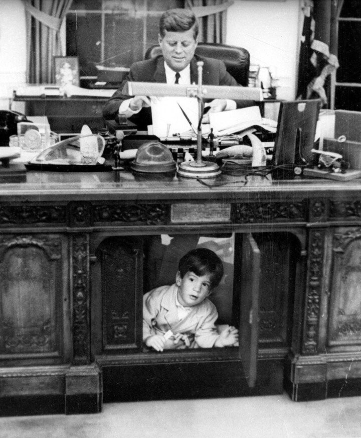 После того как Джон Ф. Кеннеди был избран президентом, Джон-младший и его старшая сестра Кэролайн часто играли в овальном кабинете Белого дома, пока папа работал. Фото 1962 года