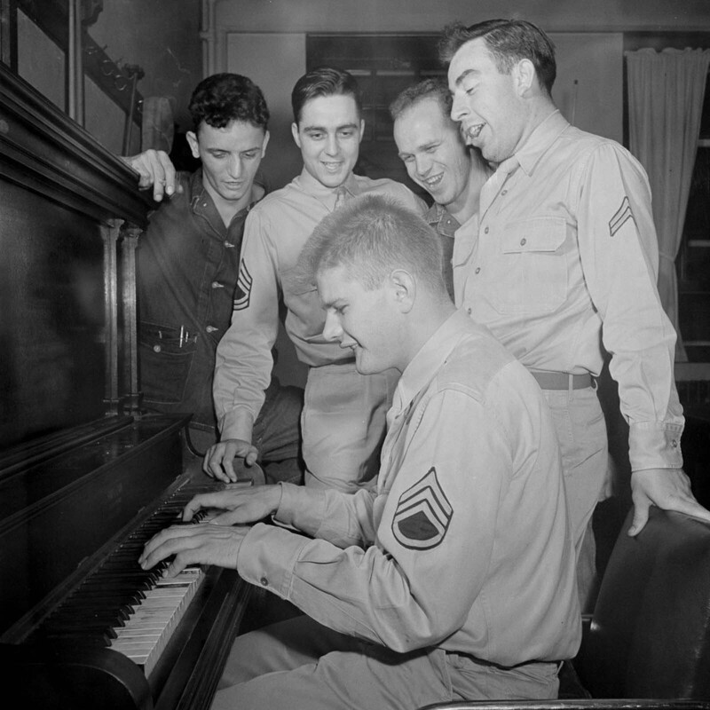 Кэмблэр играет на пианино, аккомпанируя пению своих товарищей