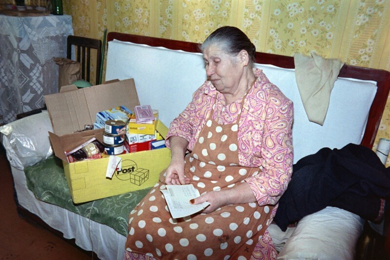 Пожилая женщина открывает в Москве продуктовую посылку с международной помощи. 9 декабря