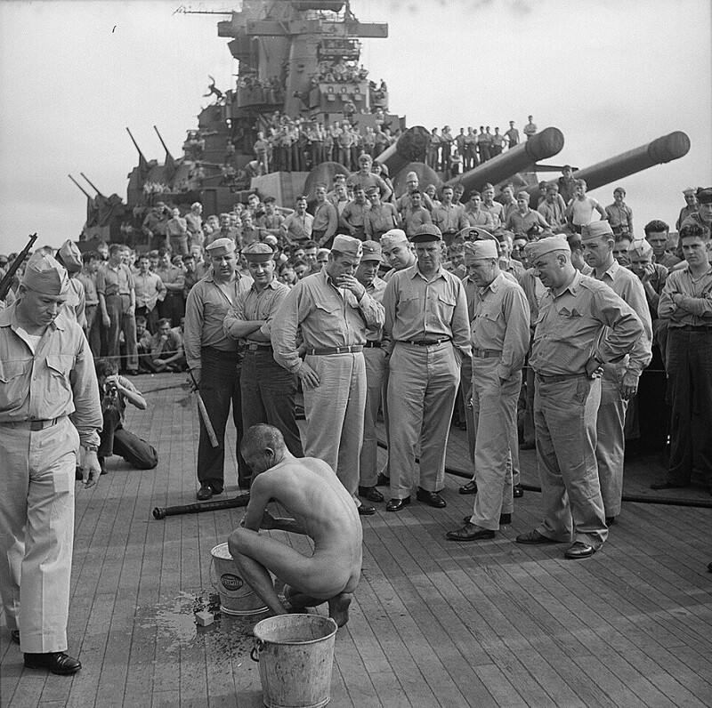 Члены команды американского линкора Нью Джерси и пленный, сбитый японский пилот-​камикадзе, которого они голым заставляют чистить палубу корабля. 1944 год