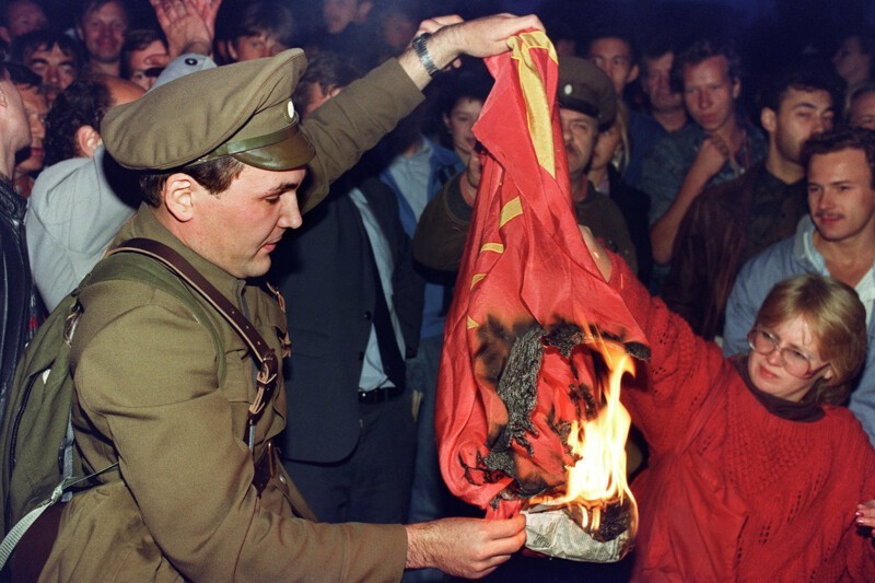  1991. Человек, одетый в дореволюционную форму, сжигает советский флаг во время митинга в Москве