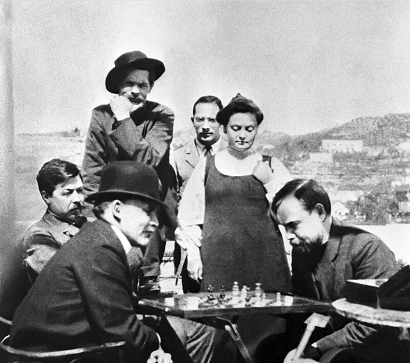 Ленин (слева) играет в шахматы с русским ученым и революционером Александром Богдановым во время посещения писателя Максима Горького (стоит в шляпе) на острове Капри в 1908 году.