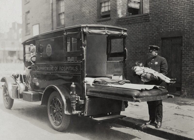 Полицейский несет больного ребенка, который находится без сознания, в машину скорой помощи, 1910 – 1920 года. 