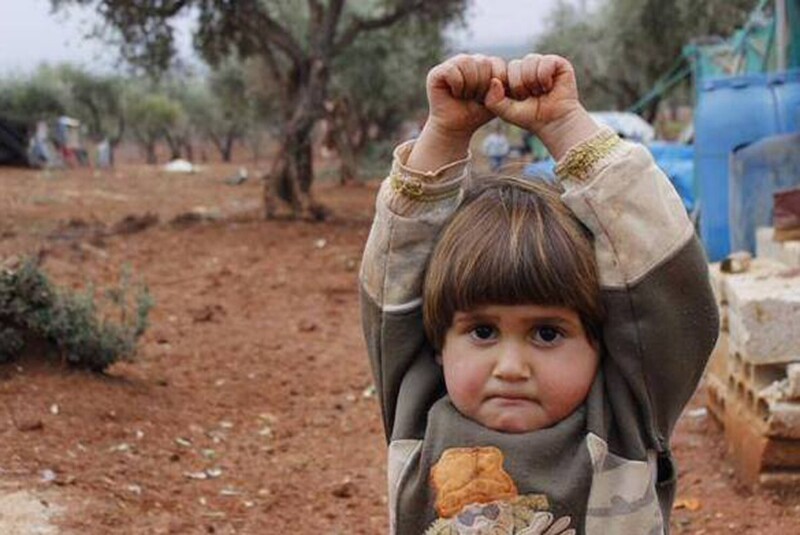 Сирийская девочка в лагере беженцев в Турции. Приняв камеру за оружие, она подняла руки вверх.