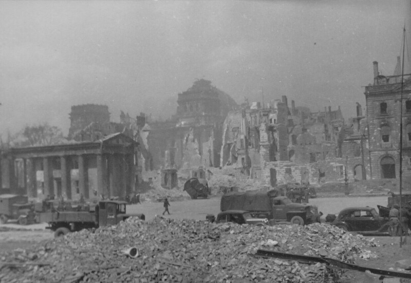 Советские грузовые и легковые автомобили на разрушенной улице Берлина. За руинами виднеется здание Рейхстага.