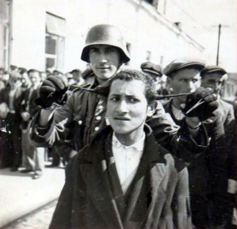 У этого еврейского юноши очень испуганный и затравленный вид, когда солдат с легкой ухмылкой показывает, что он готовится отстричь его пейсы. 1941 год
