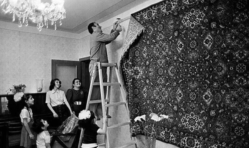 Глава семьи под восторженными взглядами своих родных прибивает к стене роскошный ковёр.