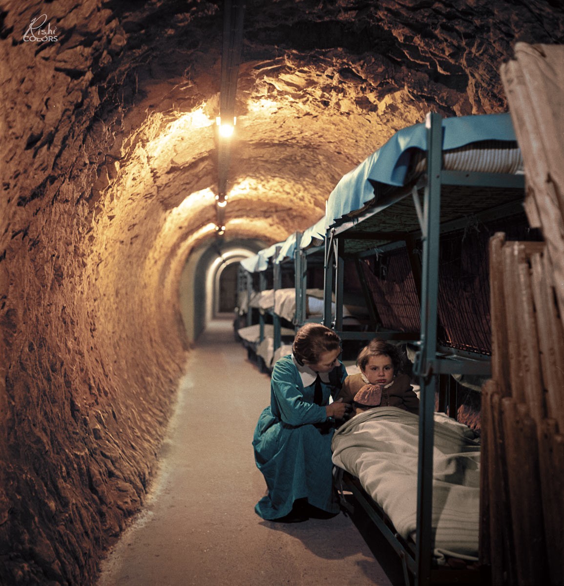 25. Женщина стоит на коленях у детской кровати в подземном туннеле во время бомбардировки Лондона. Вторая мировая война, январь 1945 года