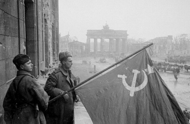 Советские военные — рядовой и лейтенант — со знаменем в Берлине на фоне Бранденбургских ворот