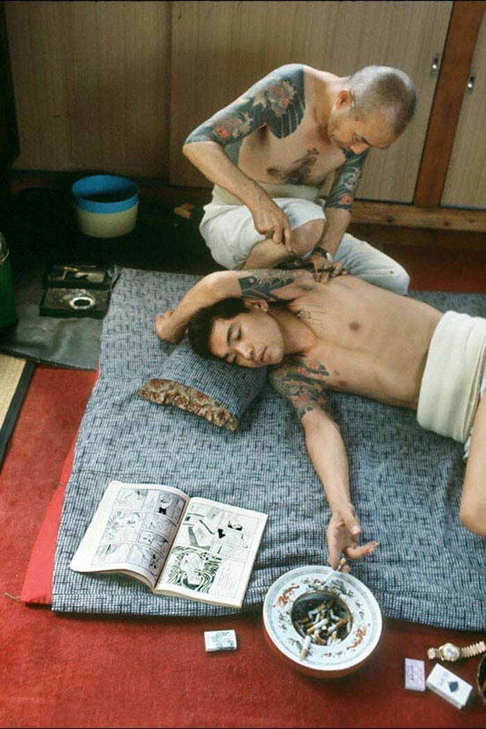 34. Мужчина курит сигарету и читает комиксы, пока ему делают татуировку, Токио, Япония, 1970 г.