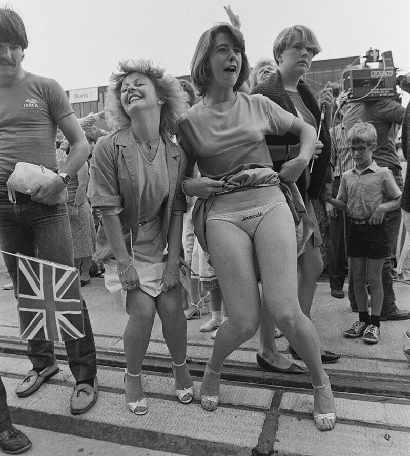 Молодая женщина со словом «Непобедимый», вышитым на ее трусиках, приветствует возвращение HMS Invincible с Фолклендов после победы Великобритании над Аргентиной в Фолклендской войне, 1982 год