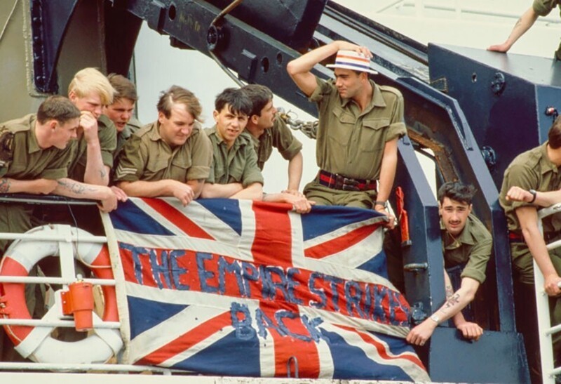 Британские солдаты отправляются на войну с Аргентиной за Фолклендские острова. На флаге надпись: «Империя наносит ответный удар». 1982 год