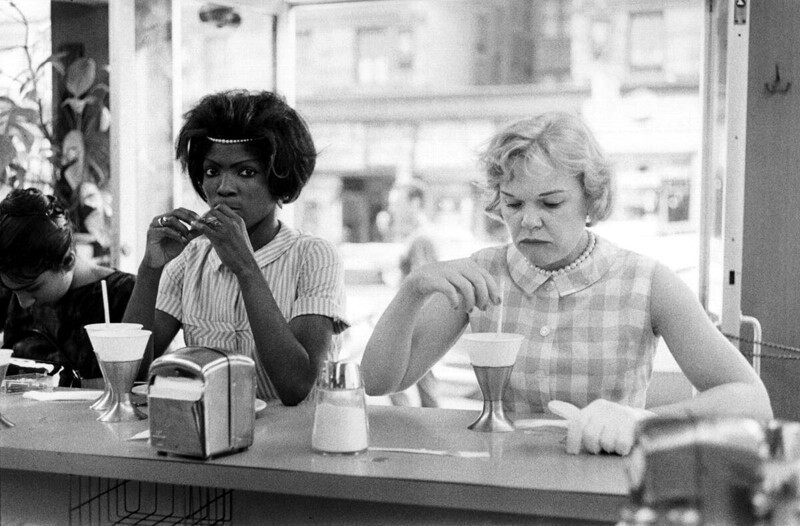 Белая женщина, всем своим видом выражает свое недовольство тем фактом, что рядом с ней за стойкой кафе устроилась черная девушка. США, 1962 год