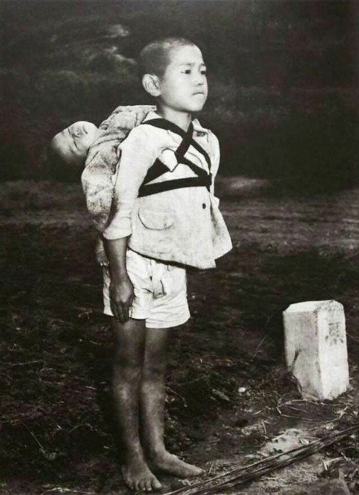 1. Нагасаки, 1945 год. 10-летний мальчик стоит по стойке смирно, принеся своего мертвого младшего брата к кремационному костру