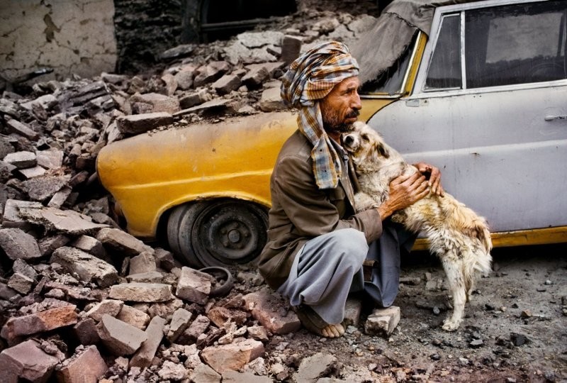 В Кабуле, Афганистан, мужчина обнимает собаку рядом со своим такси, которое было уничтожено в результате обстрела соседнего здания, 1992 год