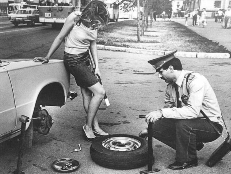 10. Сотрудник ГАИ помогает девушке заменить колесо пока она держит его жезл, 1981 год