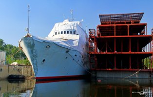 Корабль-кинозвезда ржавеет в порту Запорожья

Газета "Утро.ua"

Андрей ЛОБОДА, 30 ноября 2006, 17:52

Облезлая краска и ржавые трубы – так сегодня выглядит легендарный пассажирский теплоход "Пицунда", сменивший не одного владельца, а нынче – купленный запорожскими "металломагнатами". Кто знает как сложилась бы судьба корабля, если бы Станислав Говорухин и Борис Дуров не задействовали данный прогулочный лайнер, бороздящий воды Азовского и Черного морей, на съемках советского детектива "Пираты ХХ века". В фильме были соблюдены все каноны жанра – море, красивая природа, пираты, наркотики, любовь, карате, героизм советских моряков, гримасы капиталистического мира. Были команды хороших "наших" во главе с Петром Вельяминовым и Николаем Еременко, и плохих – "не наших", с латышскими актерами и Талгатом Нигматуллиным. Впрочем, о дальнейшем развитии сюжета рассказывать не стоит. Он известен практически всем. И не удивительно – в одном только 1980 г. в кинотеатрах СССР картину посмотрели около 87,6 млн зрителей.

Наряду с актерами известность приобрели и снятые в нем корабли. Ну как можно было забыть проход через Балаклавскую бухту красавца корабля пиратов – "Пицунду", для яркости образа переименованного в "Mercury". Построенный по заказу Советского союза в 1963 г. на верфях Болгарии, теплоход совершал круизные плавания в Крым. Не исключено что именно в одном из таких рейсов он и был замечен режиссерами одного из самых прибыльных проектов советского кинематографа.

Как известно, "ничейных" вещей, а тем более кораблей, не бывает. Для нынешних владельцев теплохода "игрушка" перестала быть актуальной и "корабль из фильма" режут на металл. Владельцы легендарного корабля хотят любым способом избавиться от груды ржавчины. По слухам, сейчас "Пицунда" даже переживает период мини-реконструкции – возможно, хозяева задумались над некоторыми предложениями от коллег-бизнесменов. Что же происходило с кораблем до сегодняшнего дня, и как он оказался в Запорожье?

После перестройки, когда практически весь транспортный флот был пущен под автоген, "Пицунде" казалось, повезло. Ее переправили в Энергодар, в качестве учебного судна для Клуба юных моряков. Откуда по прошествии нескольких лет из-за любви к отечественному кинематографу судно выкупил влиятельный запорожский бизнесмен, решивший попробовать заработать на былой славе "Пицунды". Из корабля можно было сделать плавающий ресторан или казино. Но все эти амбициозные планы так и остались планами. Сегодня "Пицунда" пришвартована в Кривой бухте, недалеко от Запорожского судоремонтного завода. Главный инженер предприятия сообщил, что судно находится в частной собственности. "А потому комментировать что-либо я не могу. Корабль стоит на частном причале, и мы к нему никакого отношения не имеем", – говорит инженер. При этом отмечает, что аналогов "Пицунде" нет и не было на территории бывшего СССР, только вот состояние у корабля плачевное.

Корабль много раз переходил из рук в руки – естественно, состояние его от такой частой смены хозяев не улучшалось. Последние владельцы ведут переговоры о том, чтобы "Пицунда" прекратила стоять мертвым грузом и, наконец, начала приносить деньги – "живая или мертвая". Некие бизнесмены хотели арендовать теплоход для международных круизов, а более меркантильные граждане предлагали, и до сих пор предлагают "распустить" легенду на металлолом. Поговаривали, что некие заезжие рестораторы сулили за аренду "Пицунды" хорошую сумму, чтобы переделать лайнер под ресторан на воде, который был бы назван в честь фильма – "Пираты ХХ века". Но видимо, что-то не сложилось, постольку ресторана нет, а ржавеющая "Пицунда" – есть.

Среди потенциальных покупателей теплохода "засветился" и губернатор Запорожской области Евгений Червоненко. Ведь Евгений Альфредович – известный почитатель не только быстрых автомобилей, но и дорогих яхт. В Крыму у главы Запорожского региона уже есть одно неплохое судно. А здесь – целый пассажирский теплоход. Еще и легендарный. Попытка подтвердить покупку "пиратского" судна губернатором Запорожской области у человека, который непосредственно занимается вопросом утилизации "Пицунды", не увенчалась успехом. "Я не хочу говорить об этом. Когда будет завершены все работы, можно будет о чем-то рассказывать. Сейчас же нам говорить не о чем".