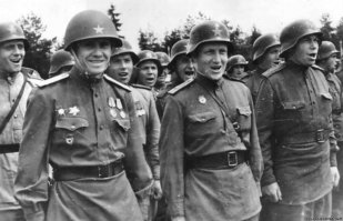 В диораме с двумя танками традиционная неточность: все красноармейцы в практически одинаковой форме и снаряжении. В повседневной фронтовой жизни все смешивалось, люди воеваи в шинелях и телогрейках, касках и шапках-ушанках, с нашим и трофейным оружием. да и в атаку с вещмешками не бежали: и груз лишний, и укрываться мешает.
Вот, кстати, фотография реального вида бойцов и командиров артиллерийского дивизиона 144-го стрелкового полка в трофейных касках на смотре в 1945 году.